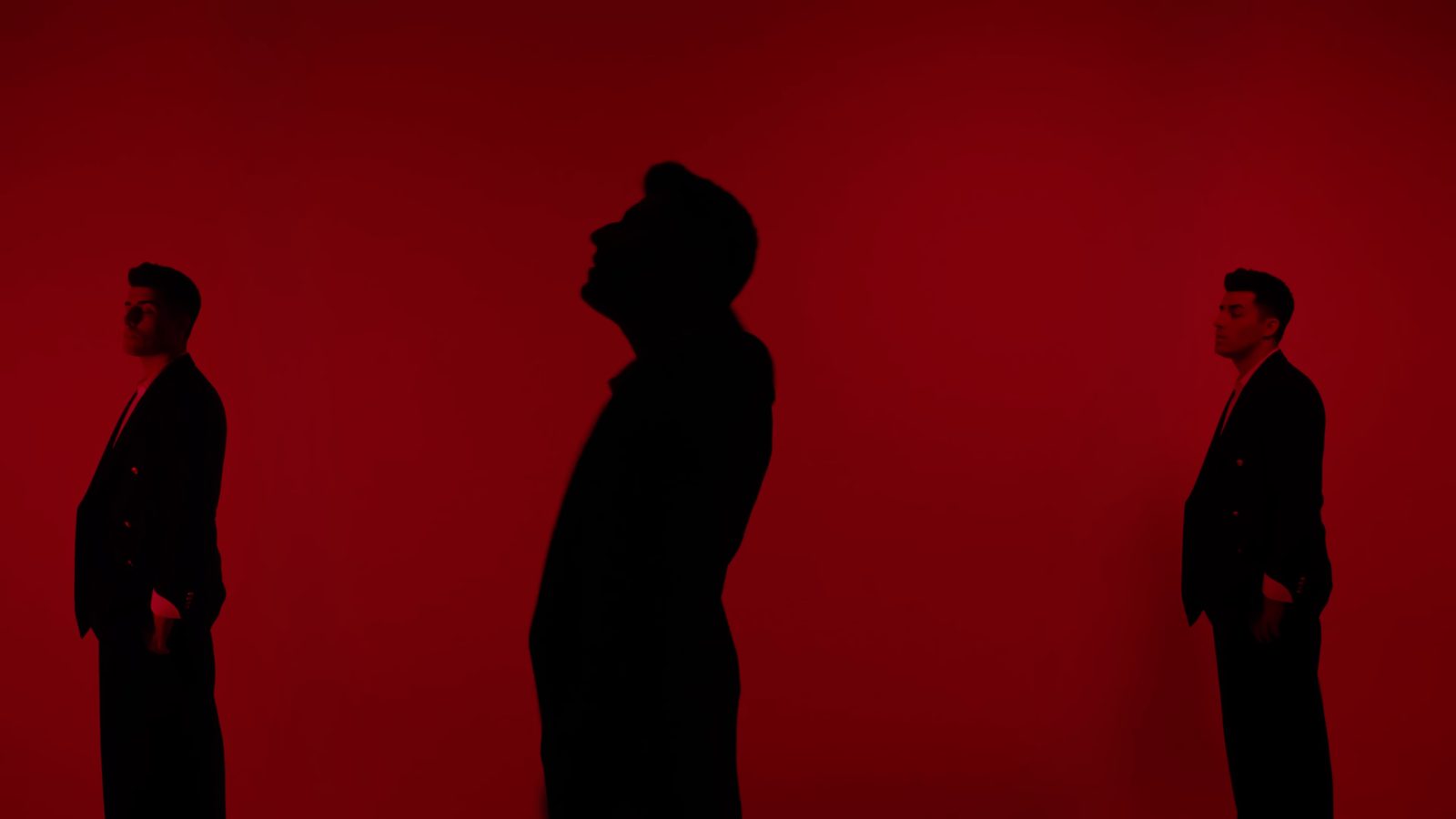 Three figures in silhouette against a red cyclorama